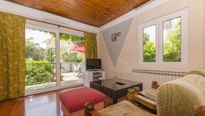 A room with a wooden ceiling, a sliding glass door to a balcony, a television on a stand, a small table, and a bed with a patterned bedspread. - Apartments Luka (Rogoznica)
