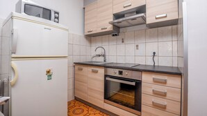 A compact kitchen with a refrigerator, microwave, sink, oven, and wooden cabinets. - Apartments Luka (Rogoznica)
