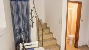 A small room with a dining table, a chair, a bottle of wine, and a blue curtain. There is a staircase leading to a bathroom with a toilet. - Apartment Marino (Moscenicka Draga)