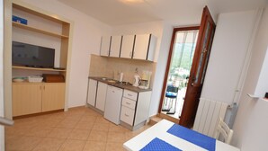 A compact kitchen with a TV, cabinets, and a dining area with a table. - Apartment Marino (Moscenicka Draga)