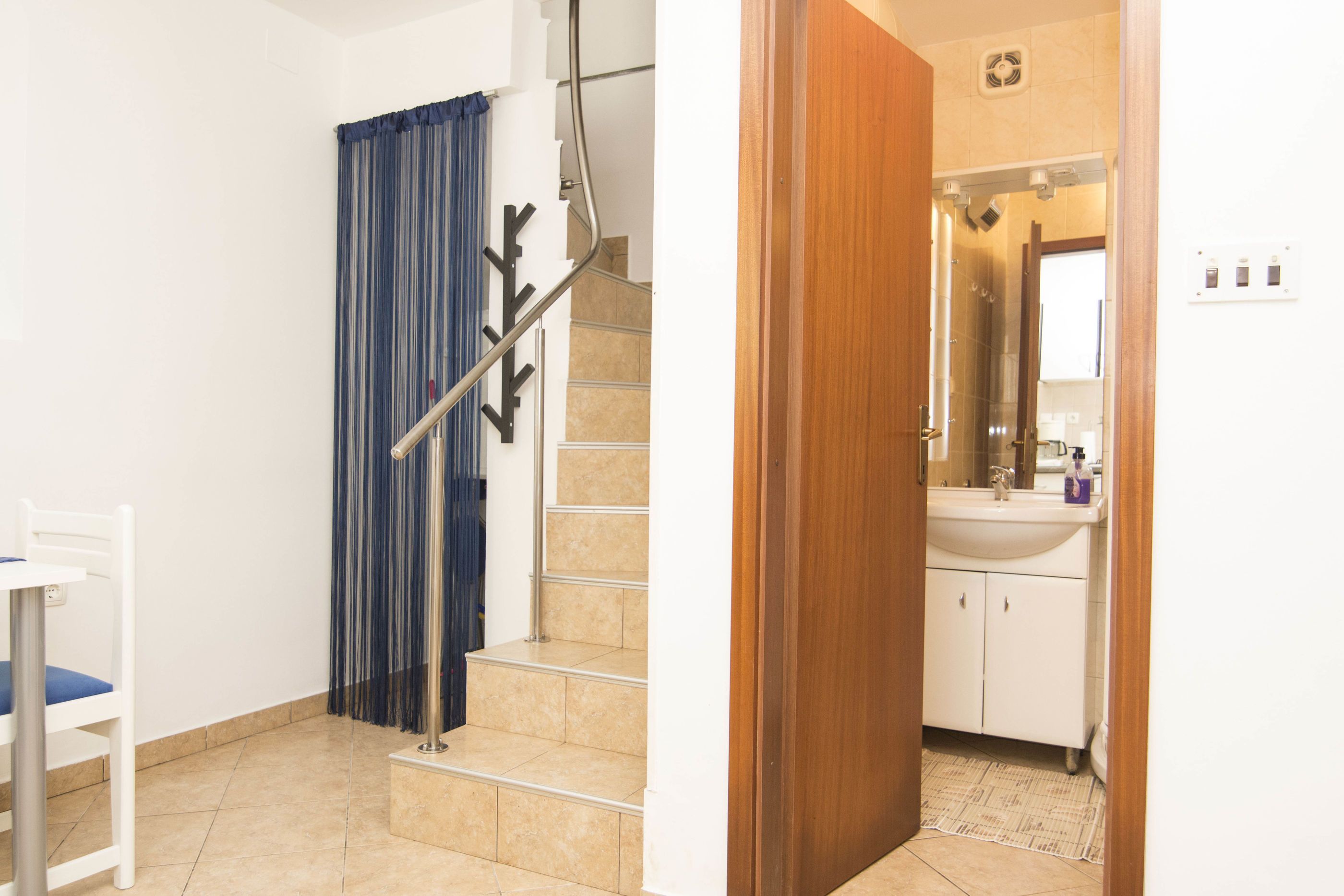 Una escalera con barandilla, una cortina azul y una silla blanca.