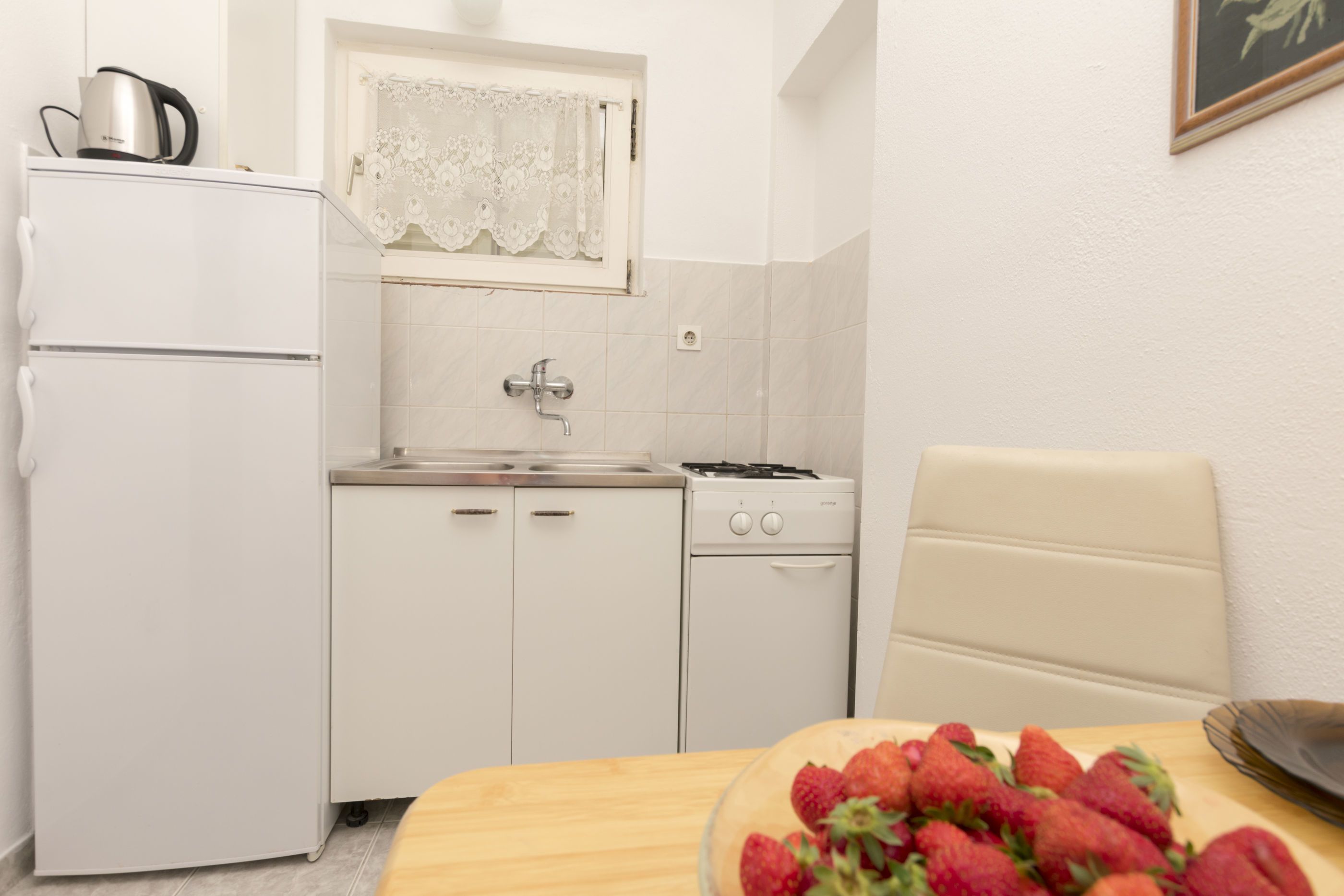 Cozinha compacta com geladeira, fogão, pia e uma mesa de jantar com um recipiente de morangos.