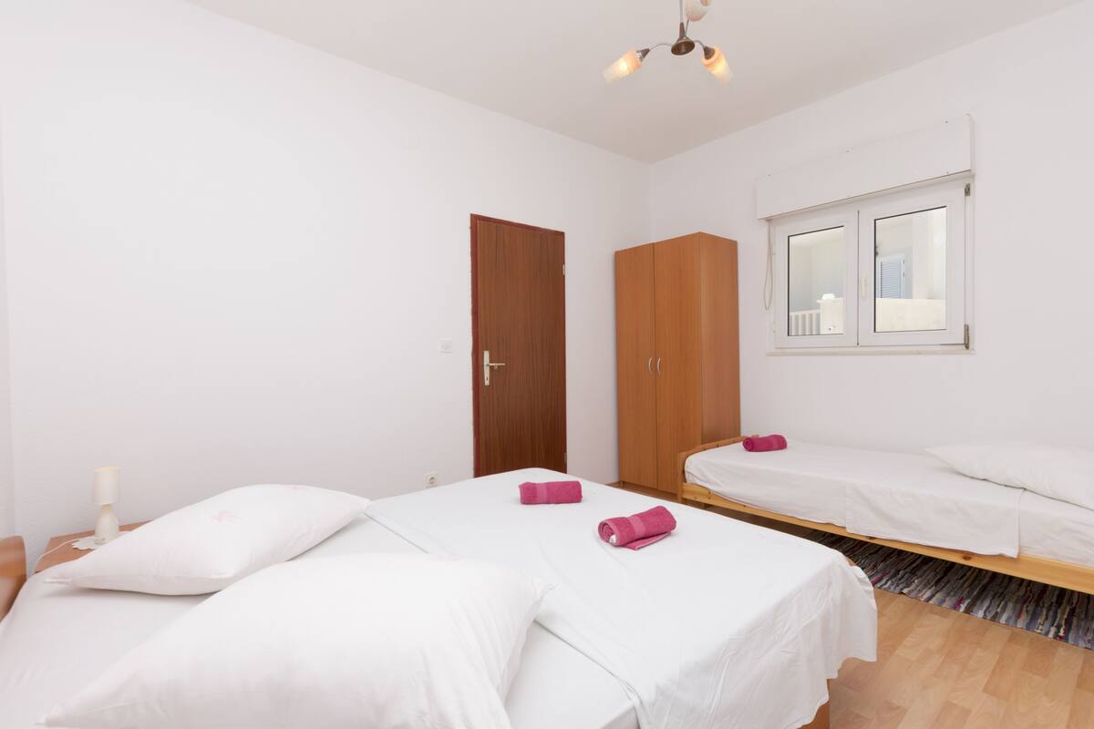 A bedroom with two beds, a wardrobe, and a window.