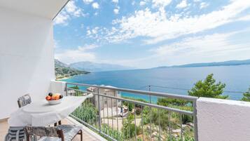 A balcony with a table and chairs, overlooking a coastal landscape with mountains and a body of water.