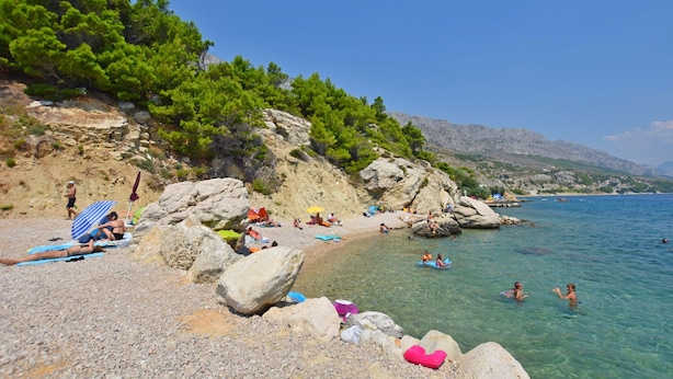 A beach with people sunbathing and swimming, surrounded by rocks and trees. - Apartments A Cappella Music (Lokva Rogoznica)
