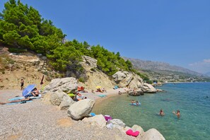 A beach with people sunbathing and swimming, surrounded by rocks and trees. - Apartments A Cappella Music (Omis)