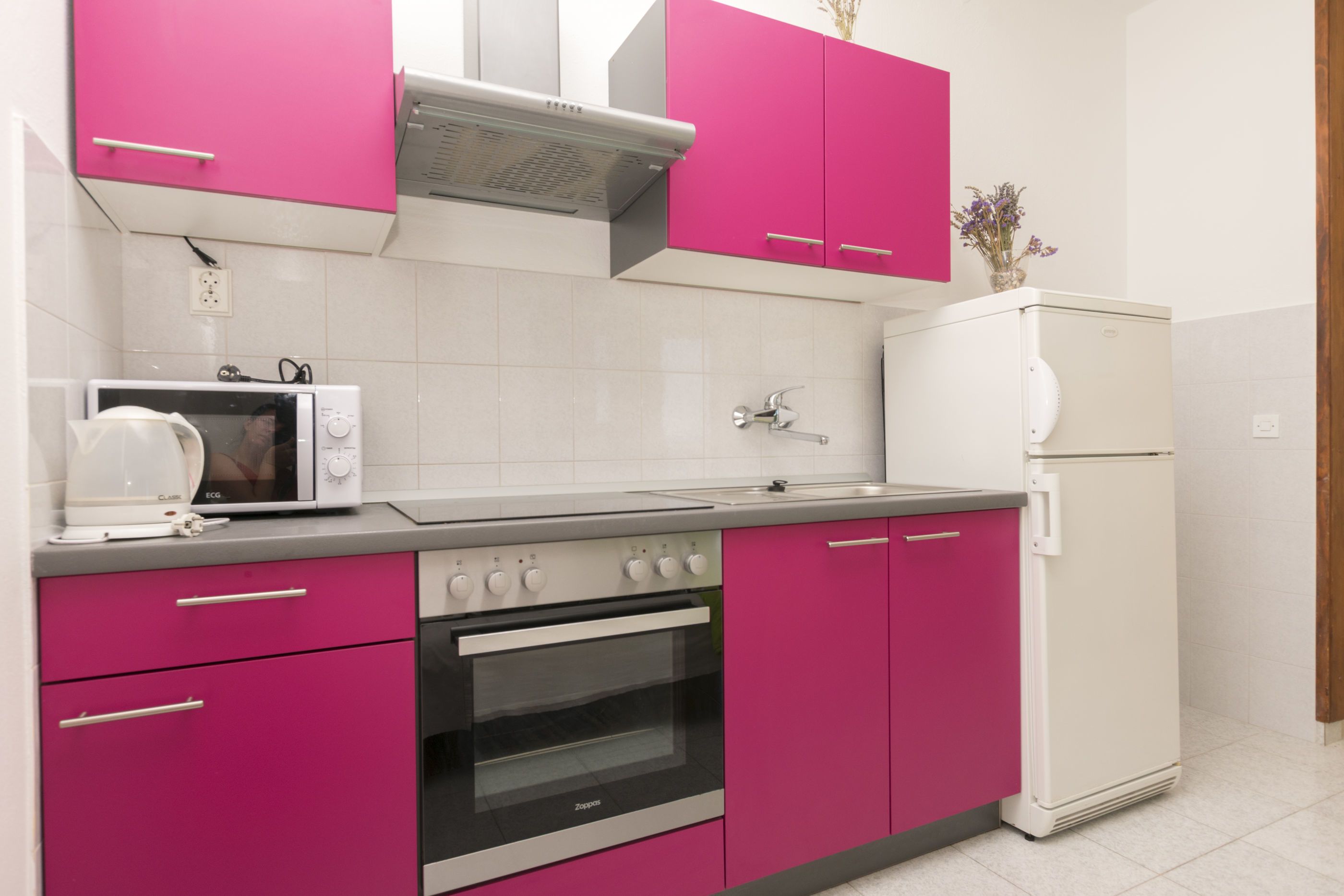 A kitchen with pink cabinets, a white microwave, a stove, and a white refrigerator.