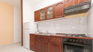 A kitchen with wooden cabinets, a white refrigerator, a stove, and a sink. - Apartments A Cappella Music (Lokva Rogoznica)