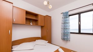 A bedroom with a bed, wooden wardrobe, a window with a view, and a hanging light fixture. - Apartments A Cappella Music (Lokva Rogoznica)