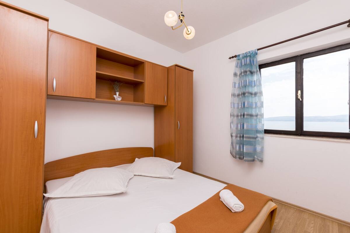 A bedroom with a bed, wooden wardrobe, a window with a view, and a hanging light fixture.
