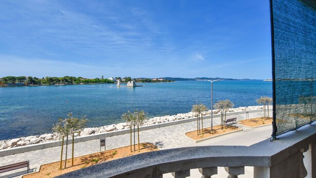 A coastal view with a clear sky, a paved walkway, and a bench. - Apartments Marica (Sukosan)