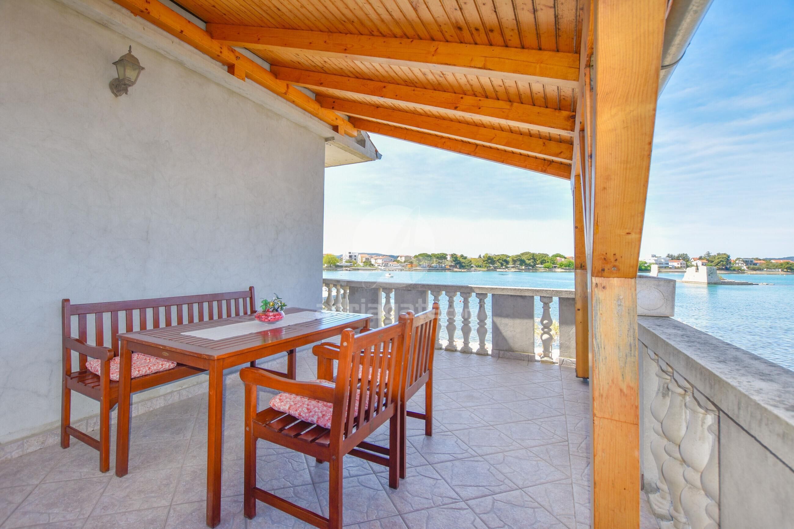 A wooden pergola with a table and chairs on a balcony overlooking a body of water.