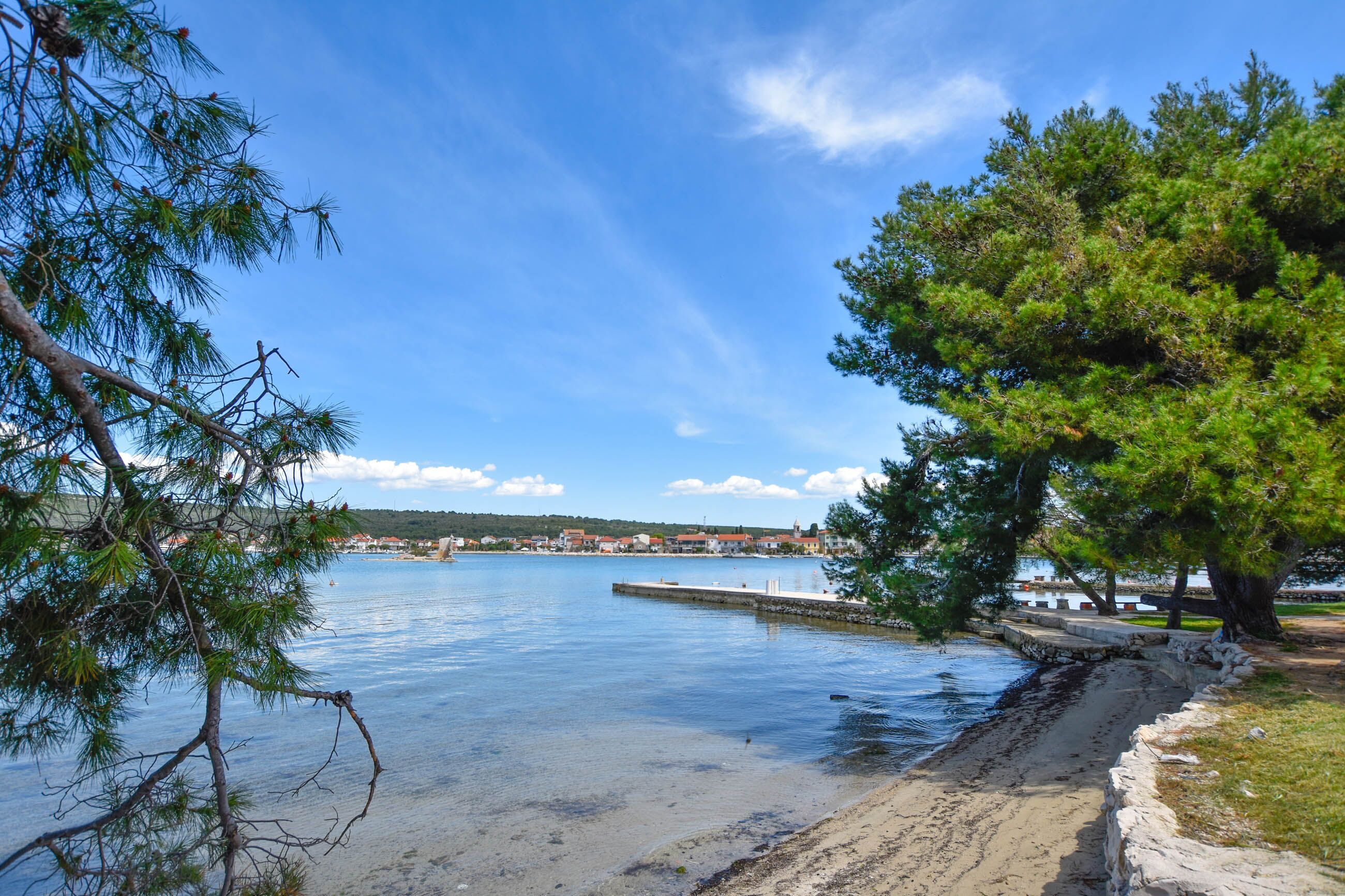 A coastal view with a clear sky, a sandy beach, and a dock extending into calm waters.