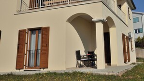 Un bâtiment à deux étages doté d’un balcon, d’une table et de chaises à l’extérieur, et d’une fenêtre avec des volets.
