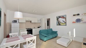 Une cuisine moderne avec des meubles blancs, un canapé turquoise et un coin repas comprenant une table et des chaises blanches.