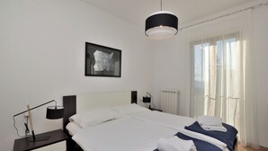 Une chambre moderne avec un grand lit, des tables de chevet, une lampe suspendue et une fenêtre avec des rideaux.