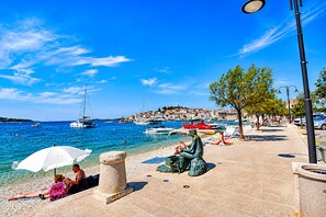 A coastal promenade with clear blue waters, boats, and a statue. - Apartments Buffalo (Primosten)
