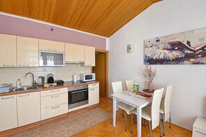 A modern kitchen with wooden cabinets, a microwave, and a dining area with a table and chairs. - Apartments Buffalo (Primosten)
