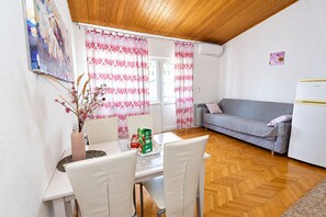 A compact living space with a dining area, a sofa, and a refrigerator. - Apartments Buffalo (Primosten)