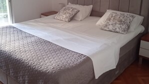 A bedroom with a bed, two pillows, a nightstand, and a window. - Apartments Buffalo (Primosten)