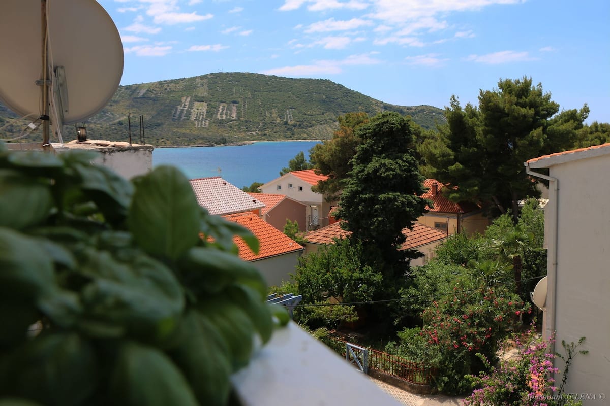 A coastal view with a satellite dish, houses with red roofs, and a mountainous backdrop.