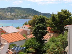 A coastal residential area with terracotta-roofed houses, lush greenery, and a view of the sea and hills in the background.