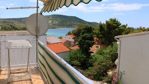 A balcony with a striped awning overlooking a coastal town, a satellite dish, and a view of the sea and hills.