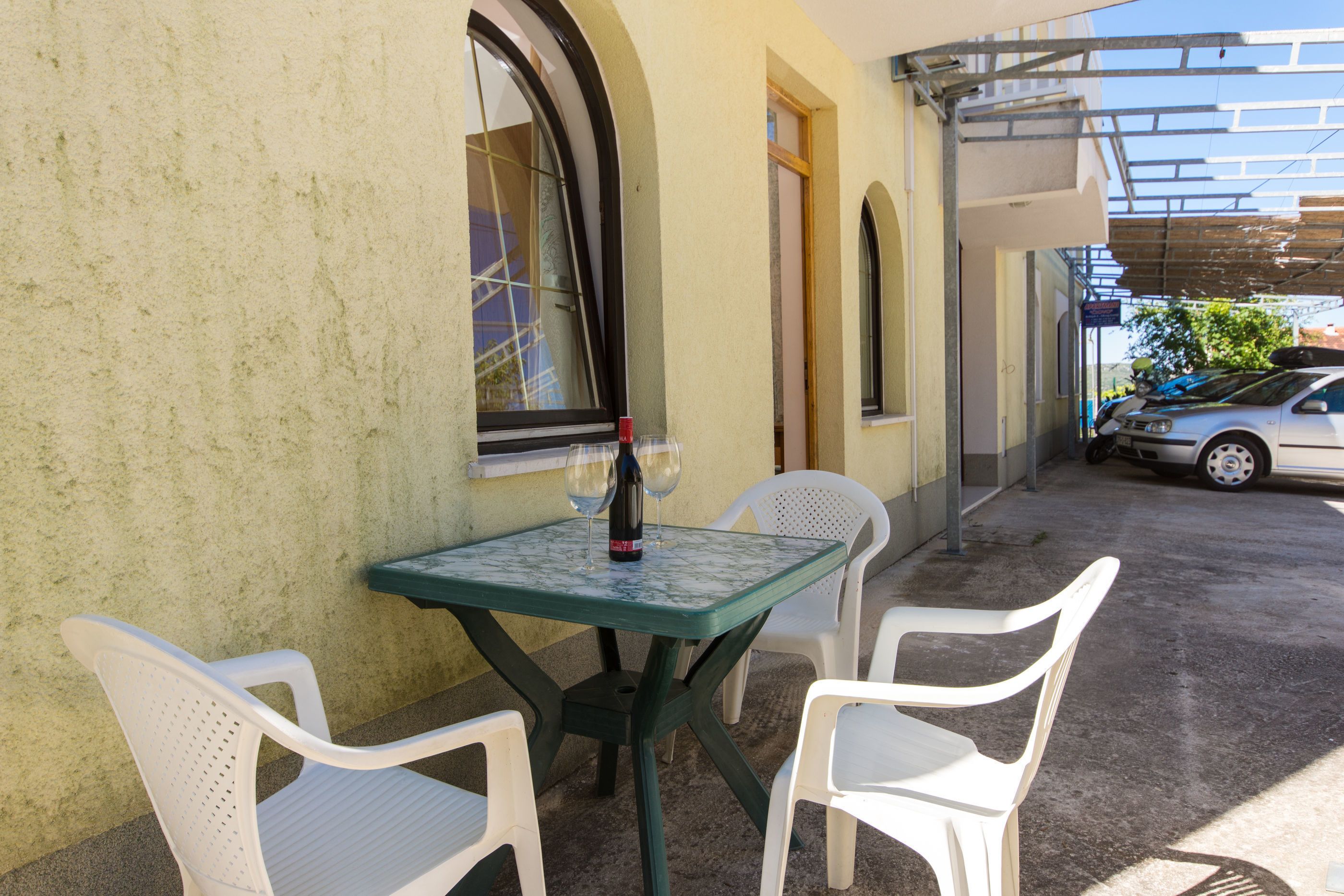 A patio with a table and two chairs, a bottle of wine, and a car parked outside.