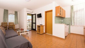 Ein gemütlicher Wohnbereich mit Sofa, kleinem Tisch, Fernseher, Holzschrank und Küchenzeile.