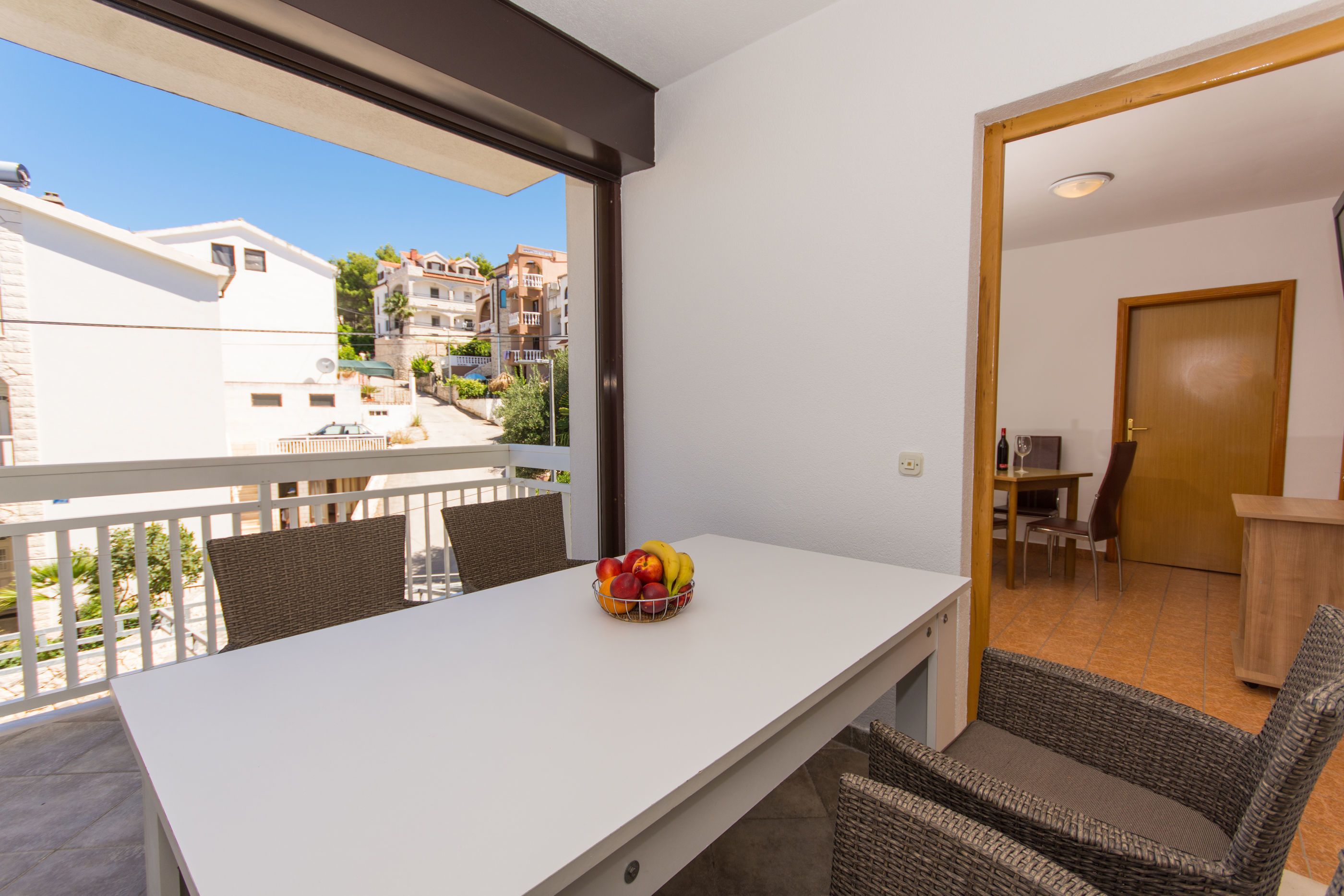 A balcony with a white table, wicker chairs, and a fruit bowl.
