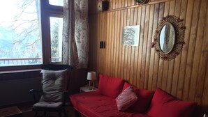 A cozy room with a wooden paneled wall, a red sofa with patterned cushions, a wooden rocking chair, a small table with a lamp, and a mirror on the wall. - Comfortable family Dupleix mountain view (Orcieres merlette)