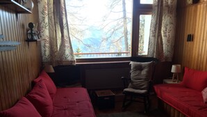 A cozy room with a red sofa, a wooden chair, and a small table. A window with a view of trees is visible. - Comfortable family Dupleix mountain view (Orcieres merlette)