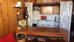 A wooden interior with a dining table, chairs, a red couch, a kitchen area with cabinets and a stove, and a wall clock. - Comfortable family Dupleix mountain view (Orcieres merlette)
