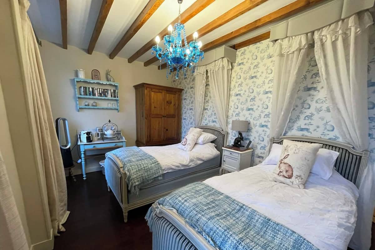 Ein Schlafzimmer mit zwei Betten, einem Holzschrank, einem Schreibtisch mit Stuhl und einer Chandelier.