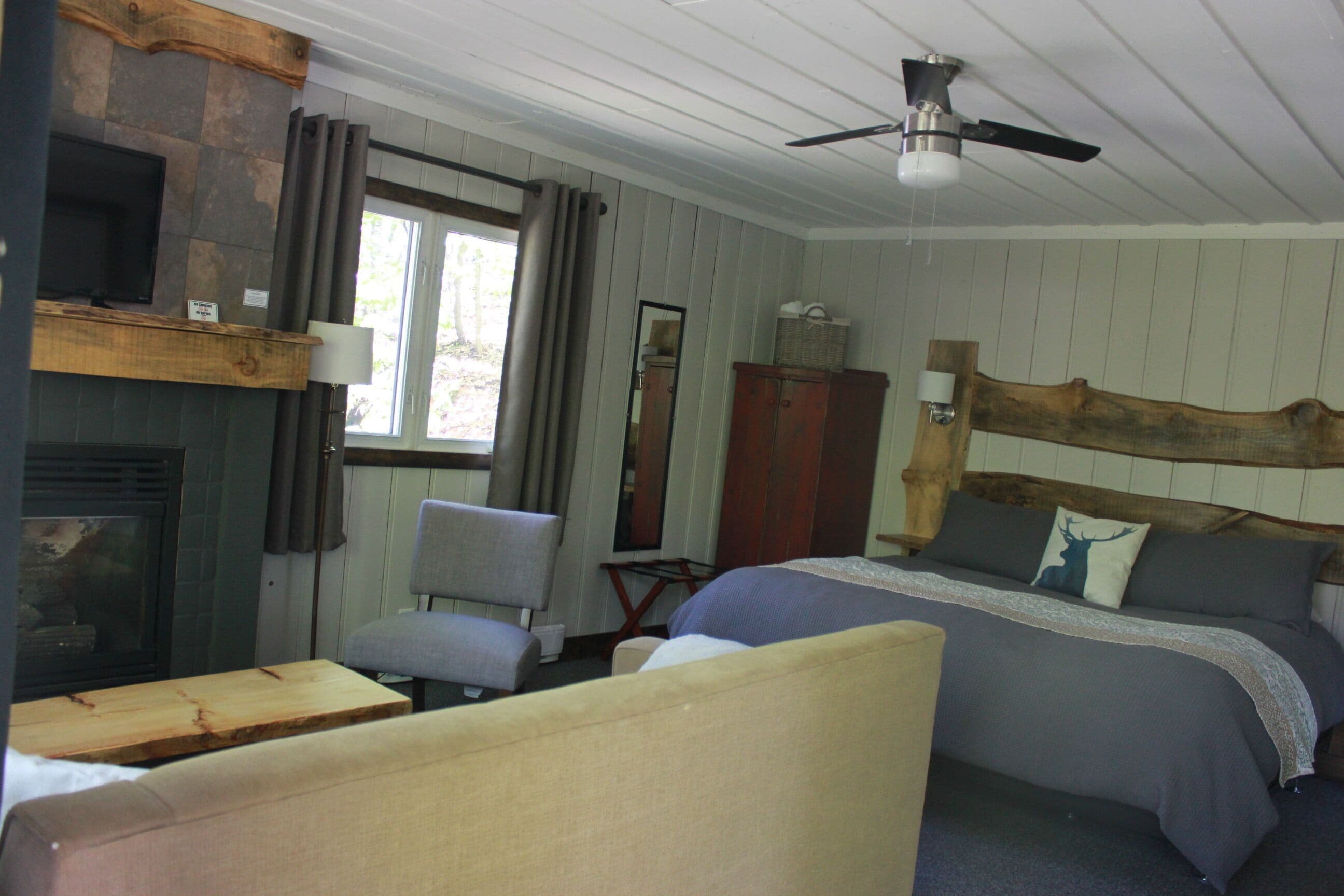 Une pièce comprenant un lit, une chaise, une table en bois, une cheminée, un miroir et un ventilateur de plafond.
