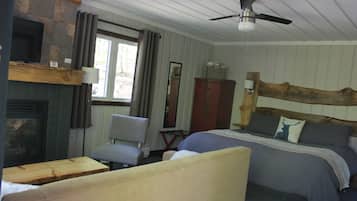 Une pièce comprenant un lit, une chaise, une table en bois, une cheminée, un miroir et un ventilateur de plafond.
