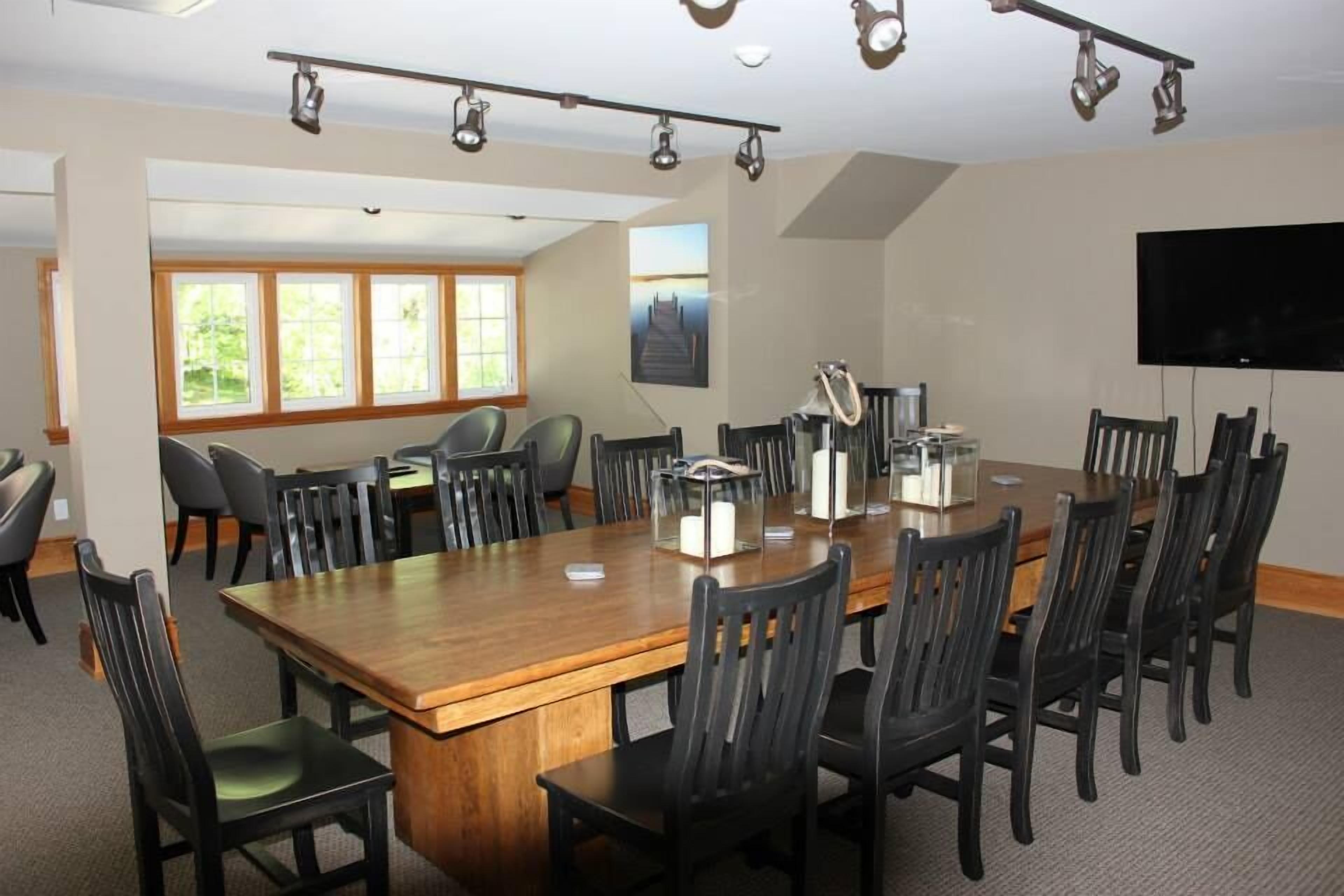 A conference room with a large wooden table, black chairs, a TV, and a painting on the wall.