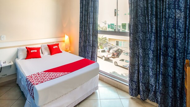 A hotel room with a bed, a bedside lamp, a window with curtains, and a view of the street outside.