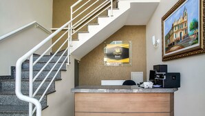 A reception desk with a sign for Dayse Hotel, a staircase with white railings, and a framed painting on the wall.