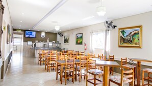A spacious dining area with wooden tables and chairs, a kitchen counter, and a television on the wall.