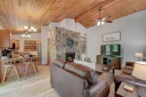 A cozy living room with a stone fireplace, a television, and a bar area with stools.