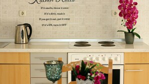 A kitchen with a tiled backsplash, a stainless steel kettle, a stove, and a potted orchid. - Apartments Mara (Supetar)