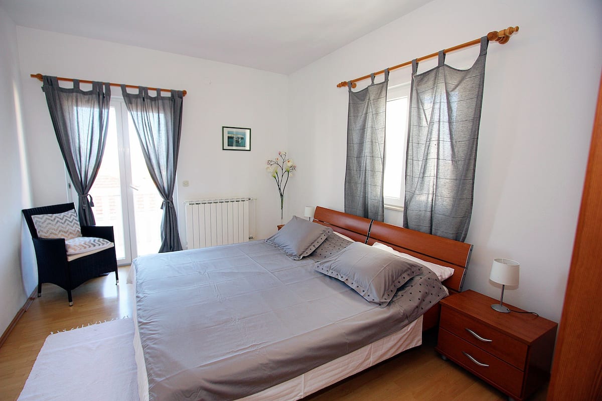 A bedroom with a large bed, a wooden nightstand, a chair, and a radiator.