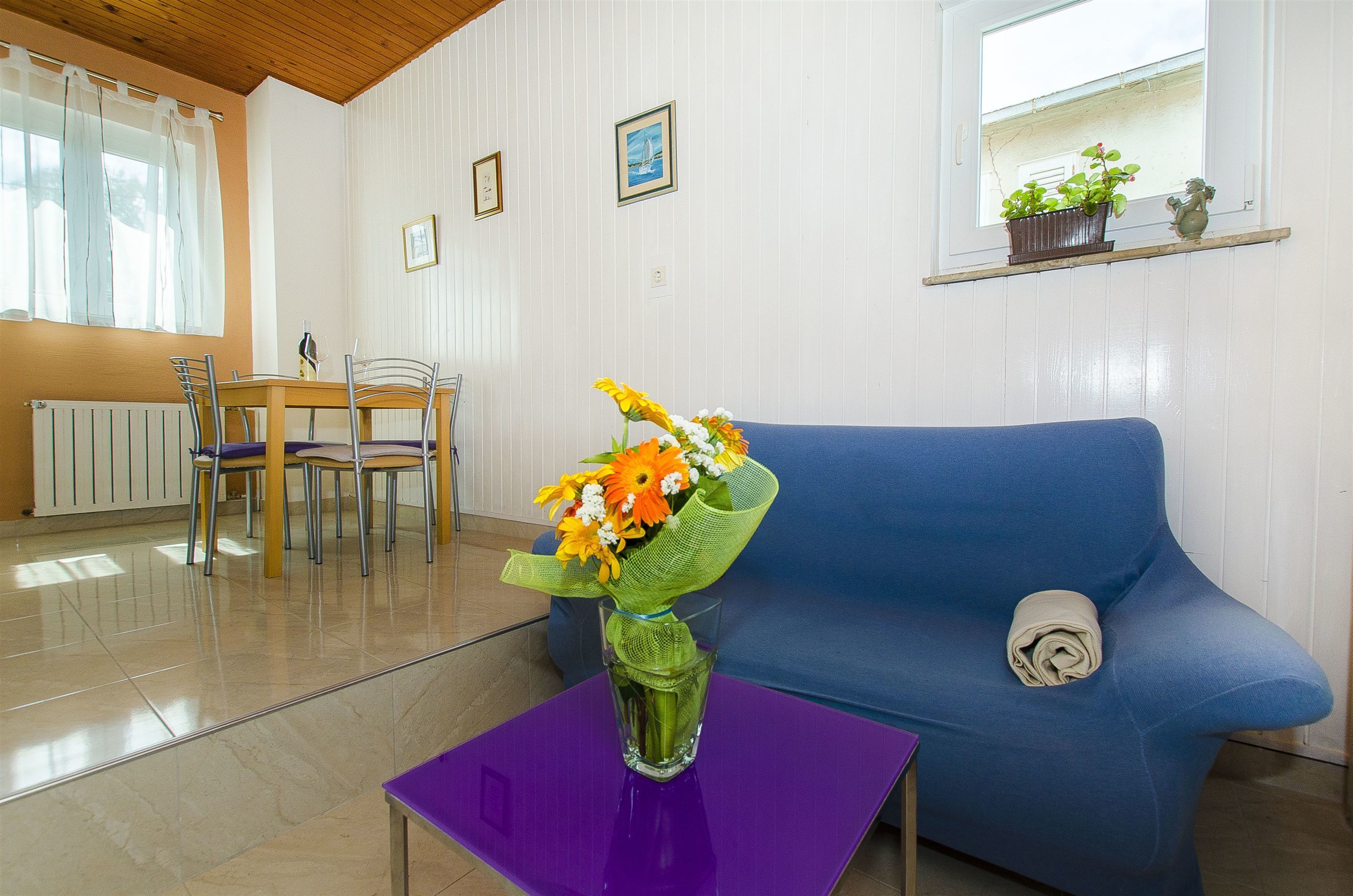 A living room with a blue sofa, a purple table, and a glass vase with flowers.