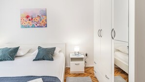 A bedroom with a bed, a nightstand with a lamp, a wardrobe, and a painting on the wall. - Apartments Jelica (Pag)