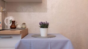 A small table with a white tablecloth, a potted plant, a coffee maker, and a pitcher on a wooden shelf. - Apartments Jelica (Pag)