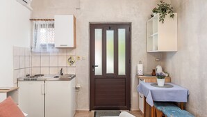 A compact kitchen with a refrigerator, stove, and sink. There is a wooden bench with a table and a potted plant. - Apartments Jelica (Pag)