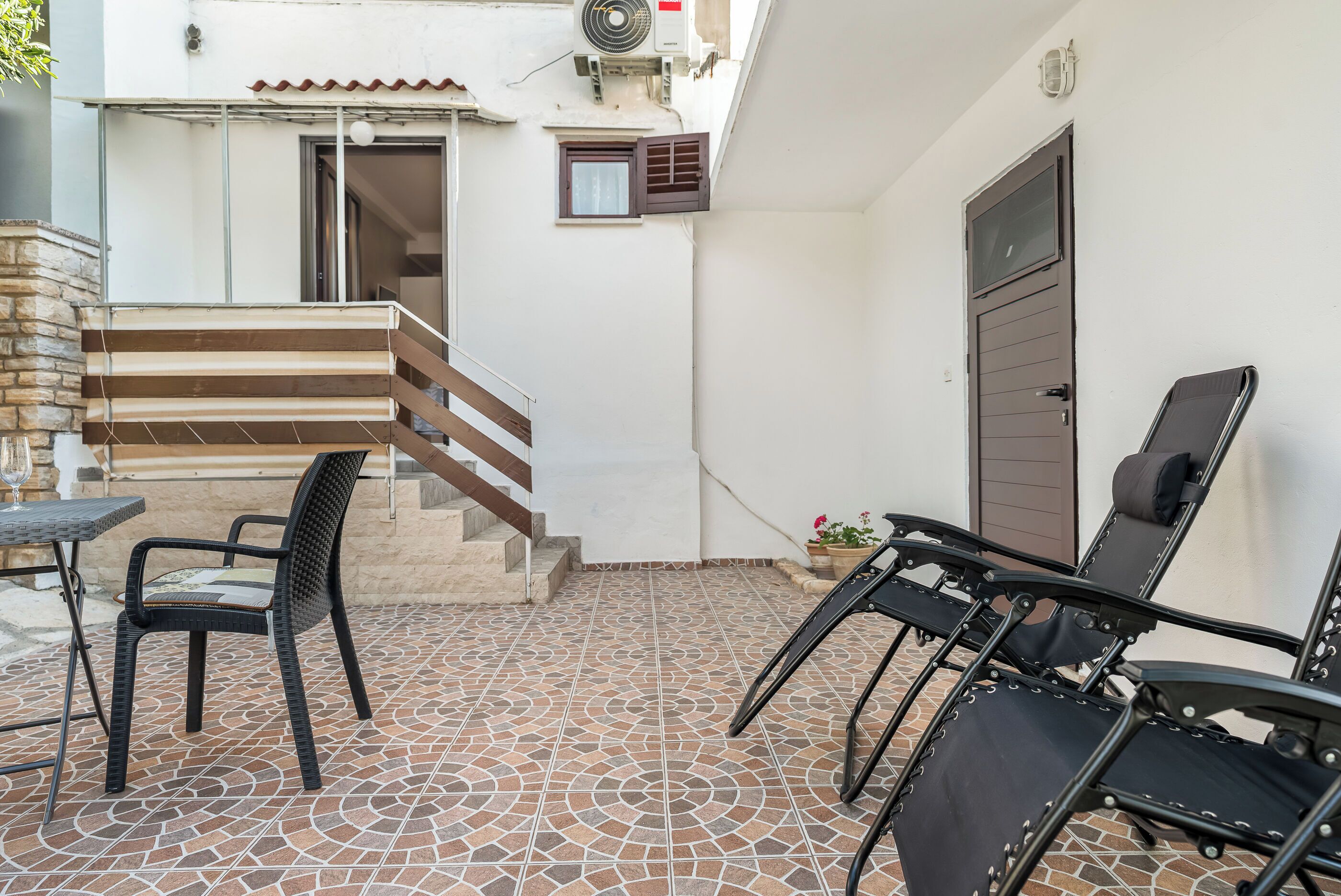 A patio area with a tiled floor, a table with chairs, a staircase, and a door.
