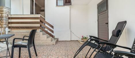 A patio area with a tiled floor, a table with chairs, a staircase, and a door.