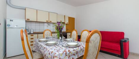 Ein Essbereich mit einem Tisch, gedeckt für vier Personen, umgeben von Stühlen. Im Hintergrund ist eine rote Couch zu sehen.